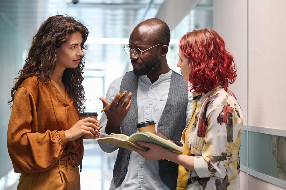 Three colleagues exchanging ideas and insights in an office hallway.