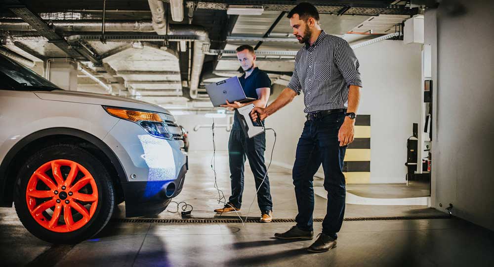 In a garage, two men stand next to a car, highlighting their focus on quality and safety.