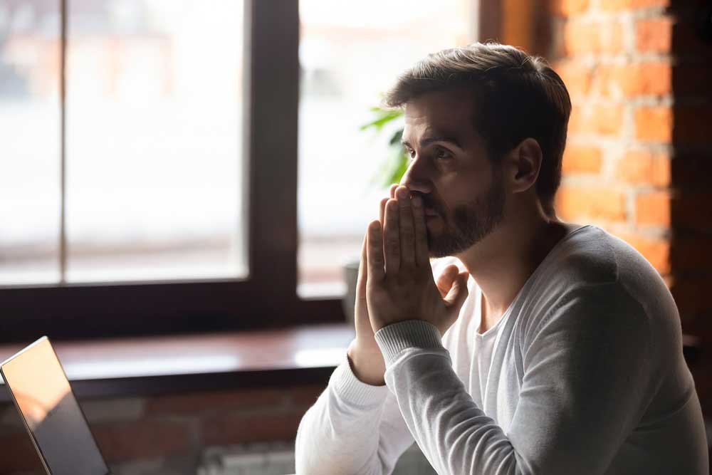 A man sits at a desk, resting his chin on his hands, deep in thought or contemplation.