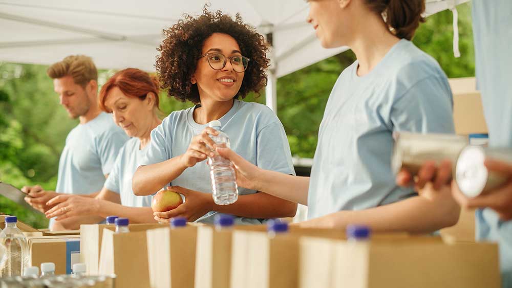 Individuals stand together around boxes and bottles, participating in a charitable donation activity.