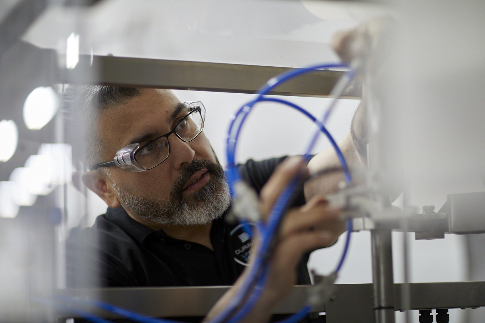 A man with glasses and a beard is engaged in operating a machine, demonstrating expertise in a technical workspace.