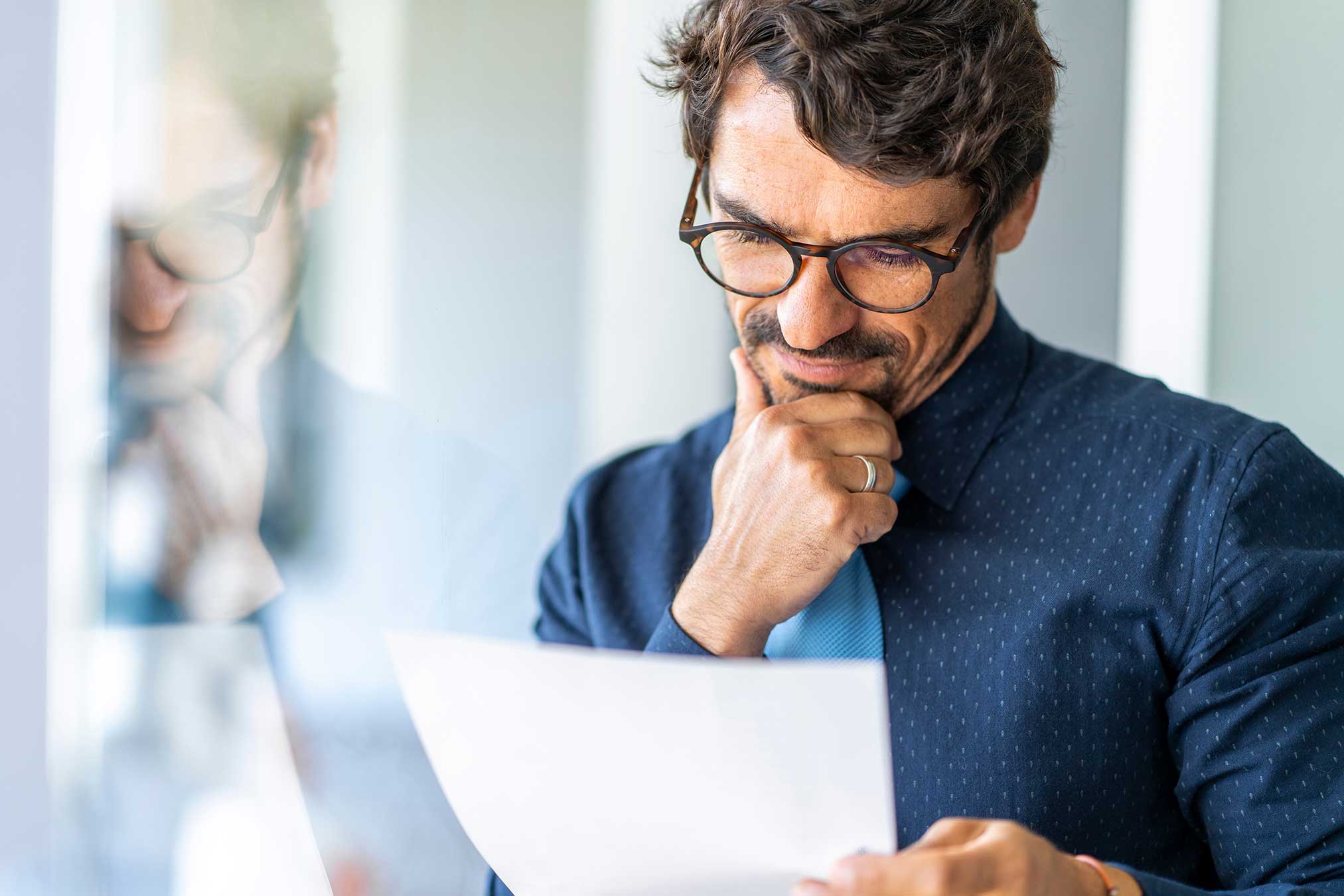 A man wearing glasses examines a document, focusing his attention on the information presented