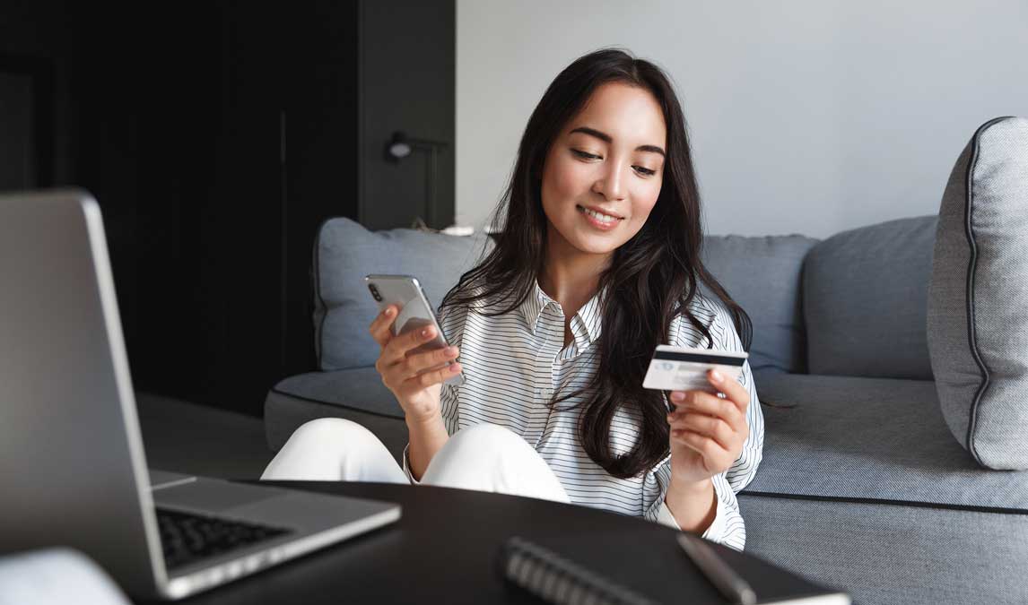 A woman sitting on the floor in front of a laptop on a table, holding a gift card