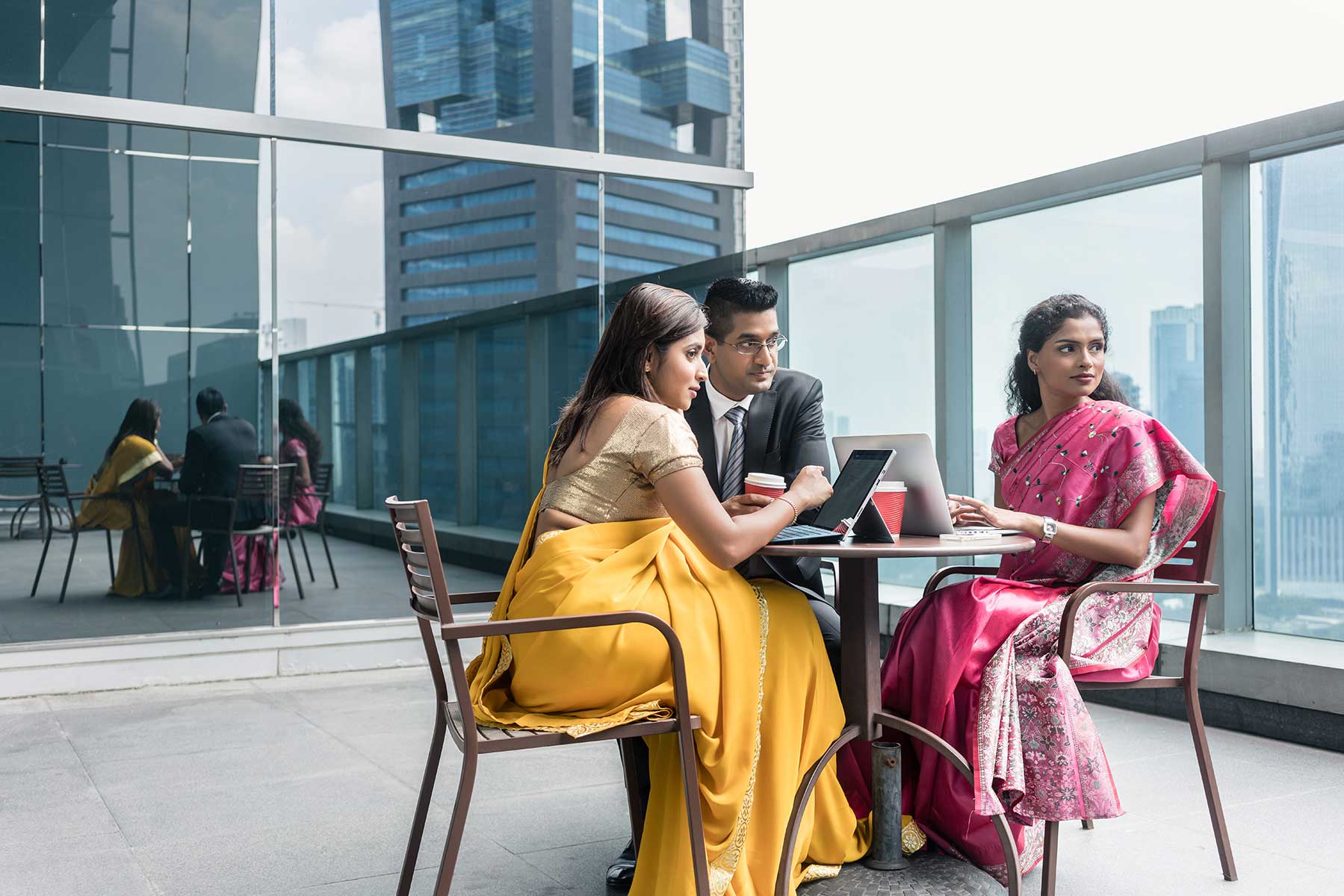 Two women in colorful saris sitting at a table with a male colleague