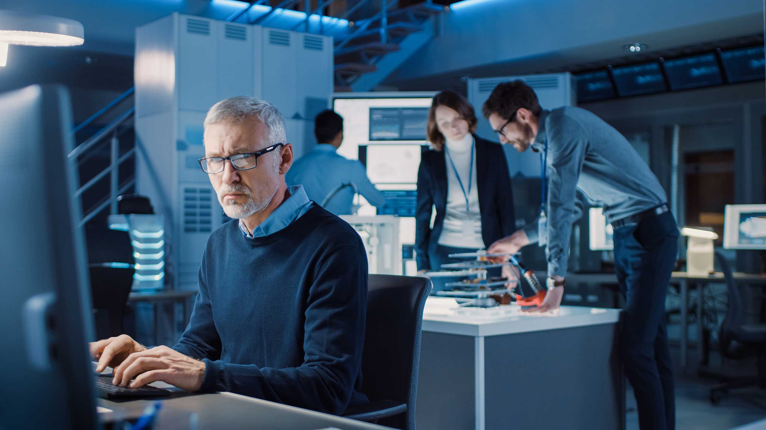 A man focused on his computer in a room with other people