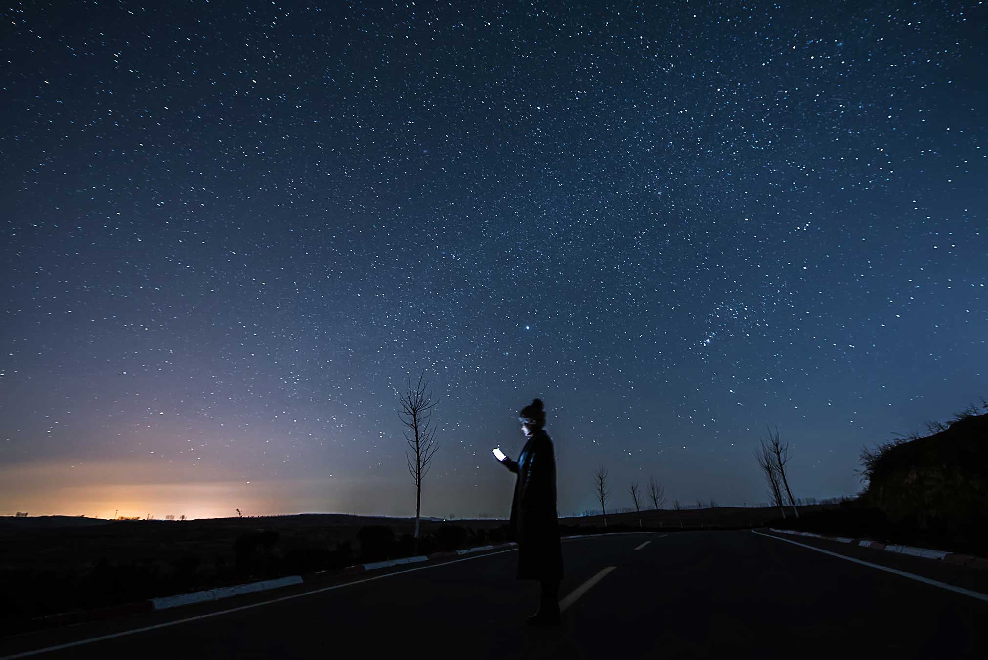 A person standing in the road, gazing up at the sky