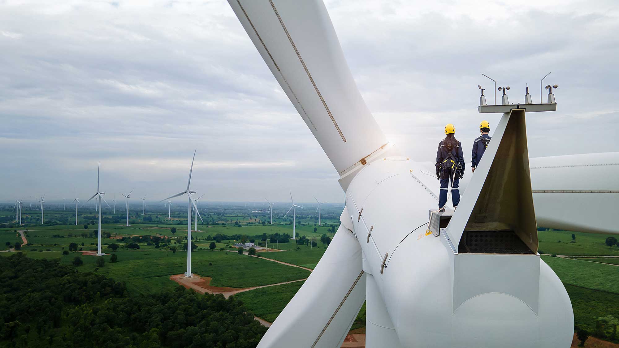 Two people standing on top of a wind turbine