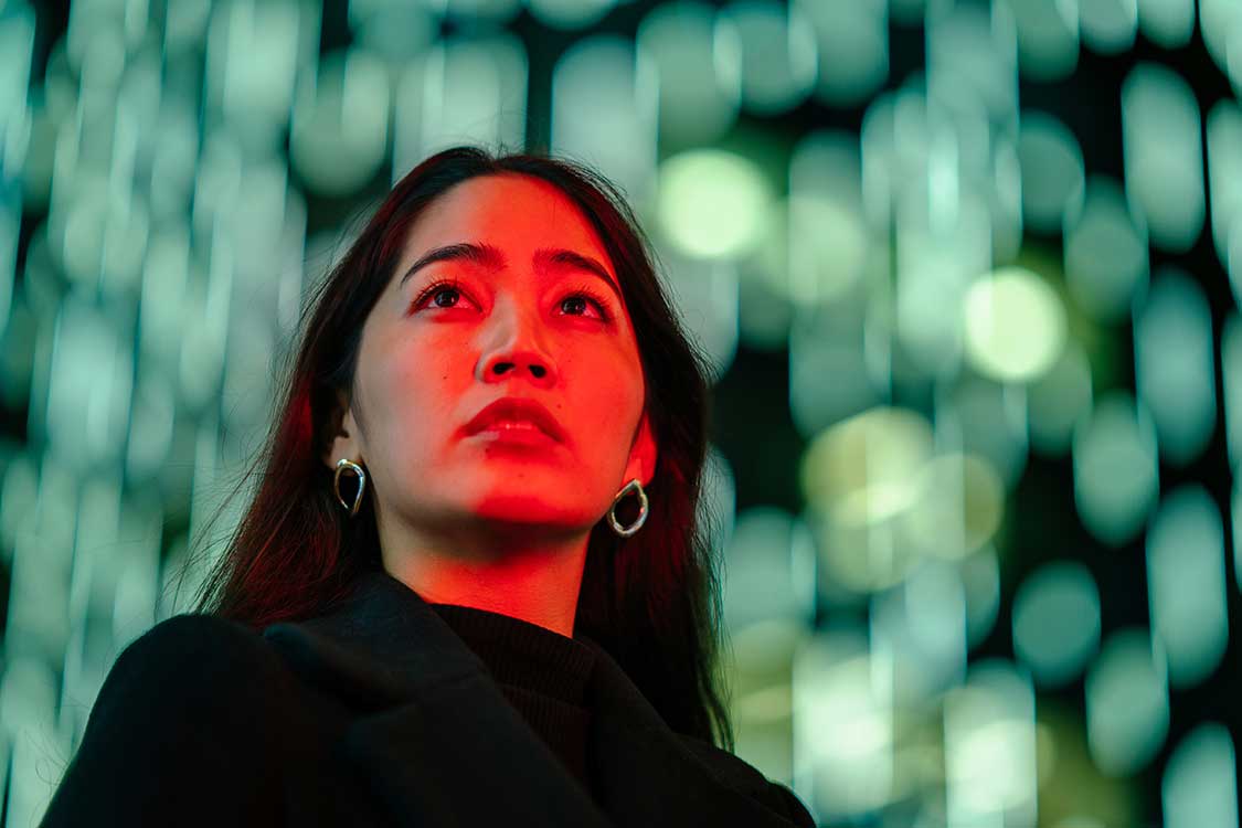 A woman gazes at the sky with radiant lights illuminating the background